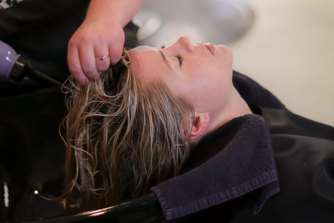 Parrucchiera che applica colpi di sole su capelli castani con pennello e ciotola di decolorante, utilizzando il metodo delle ciocche selezionate
