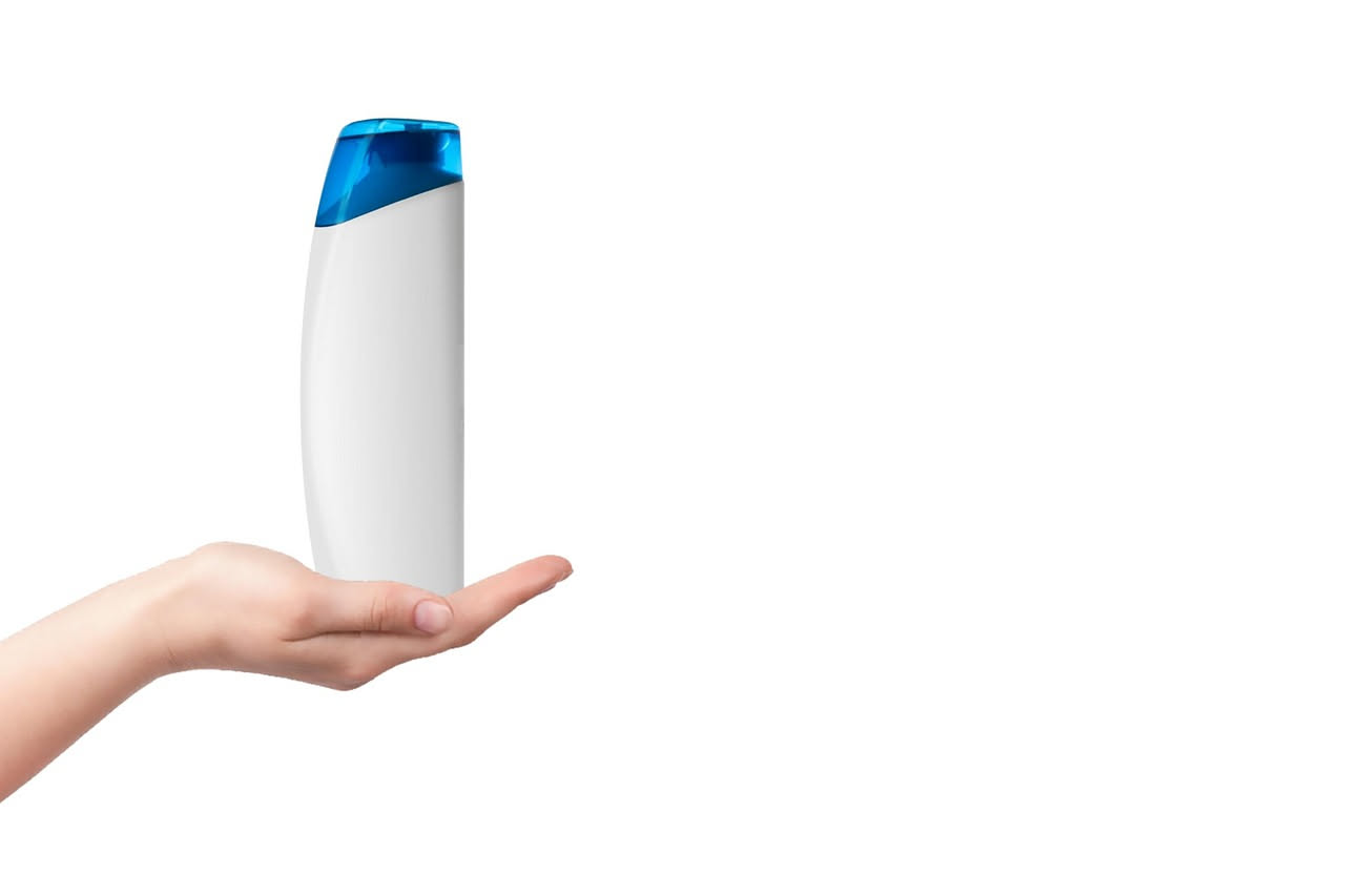 Bottiglia di shampoo delicato traslucido e bottiglia di shampoo chelante di colore più intenso poste una accanto all'altra su sfondo bianco, con bolle di schiuma intorno