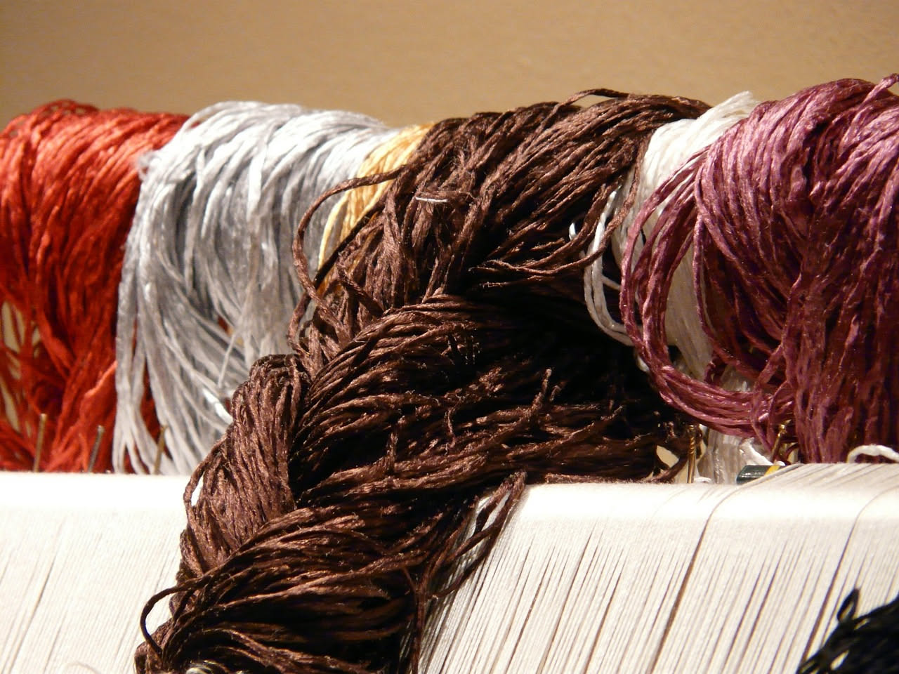 Dettaglio di una federa di seta color champagne accanto a una di cotone bianco, con una ciocca di capelli castani ondulati posizionata su entrambe le superfici per mostrare la differenza di riflession