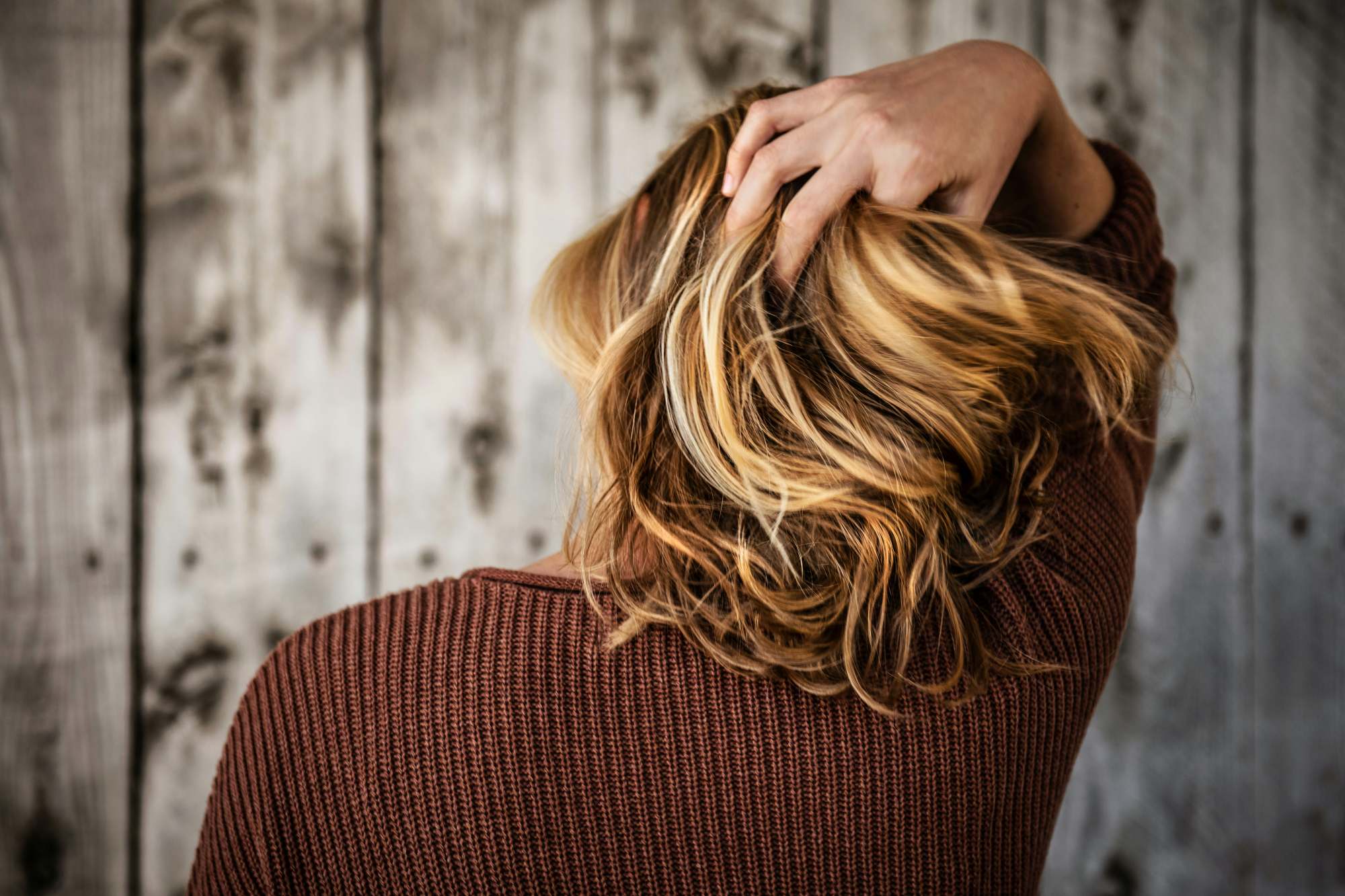 Ragazza con capelli lunghi castani bagnati di sudore in giornata estiva soleggiata, che si tocca la radice dei capelli al cuoio capelluto