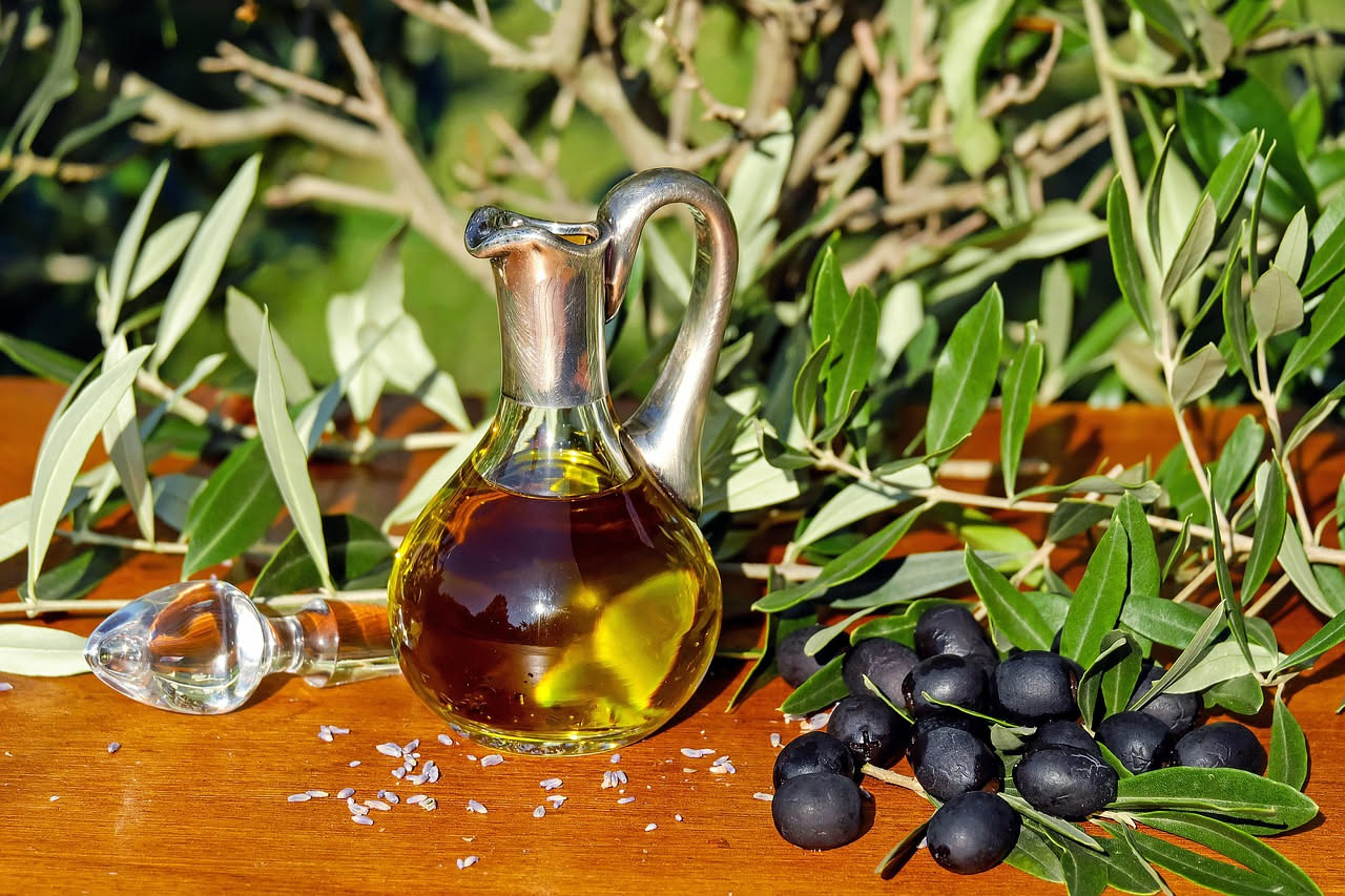 Donna con capelli lunghi e brillanti riceve un trattamento di olio di oliva, con una bottiglia di vetro scuro sullo sfondo e ulivi sfocati
